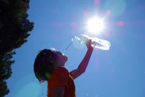 Low angle view of child pouring water in mouth, sun in background.